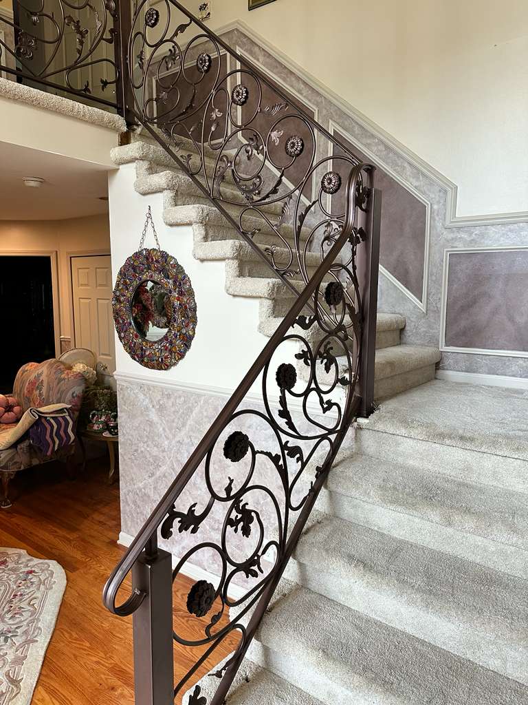 Ornate wrought iron staircase railing with decorative scrollwork in a luxury home, custom fabricated by Hot Fab Welding in Warren, MI
