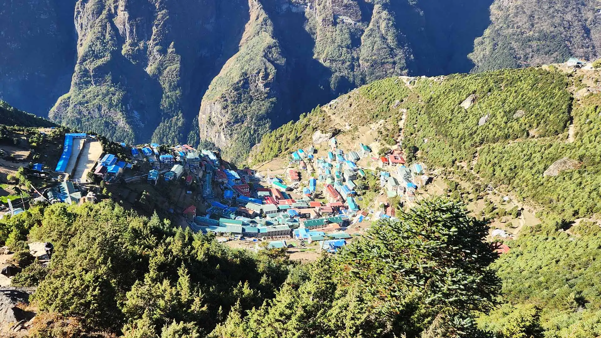 Colorful rooftops cluster in a hillside village surrounded by forests and steep mountain slopes.