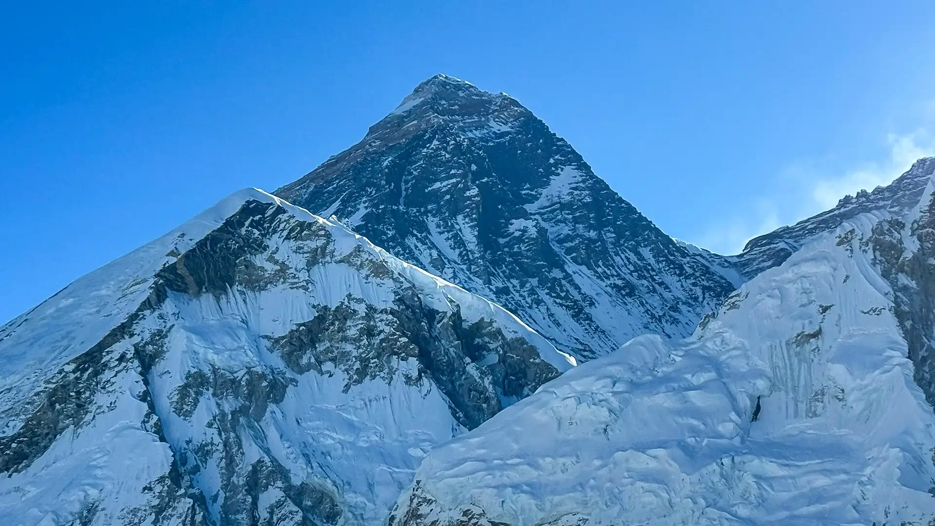 Mount Everest rises behind snow-covered ridges and fractured glaciers beneath a clear blue sky.