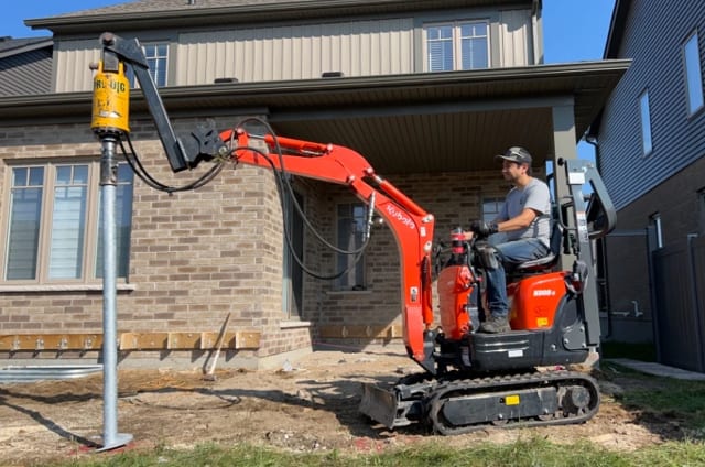 Helical pile installation with excavator on residential site