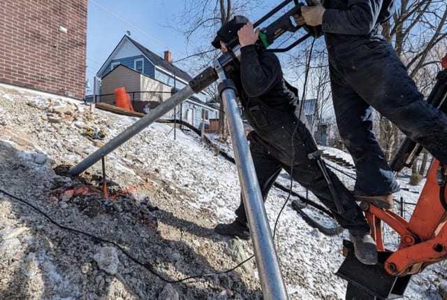 Installer driving helical pile into soil