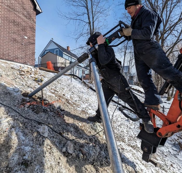 Installer operating helical pile machinery in winter conditions