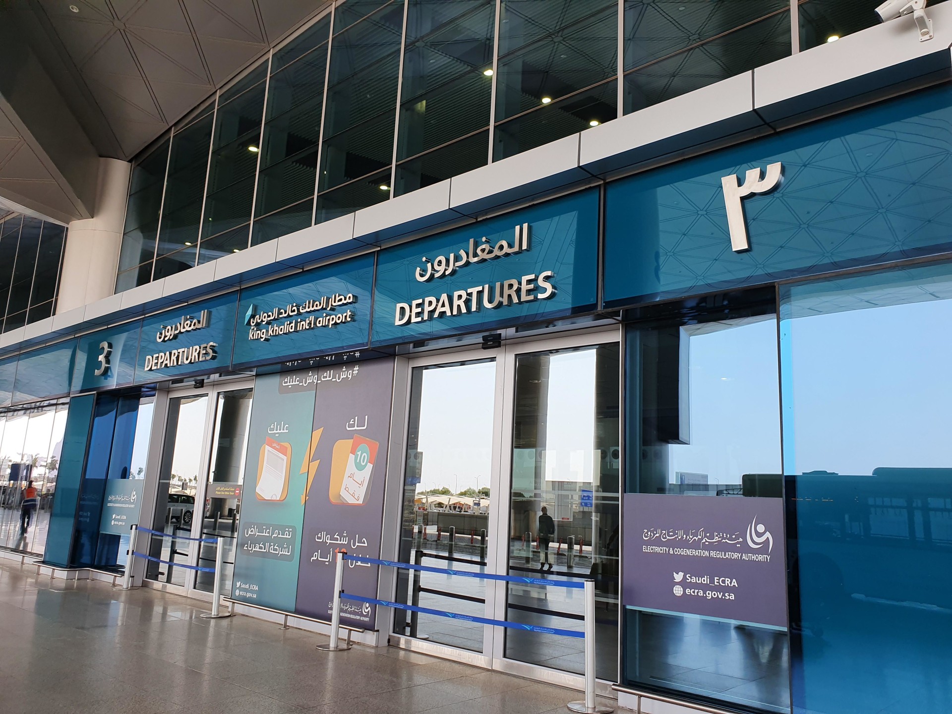 The departures entrance at King Khalid International Airport in Riyadh, Saudi Arabia, photographed in August 2019. The archival image shows the terminal's glass facade and bilingual departure signage.