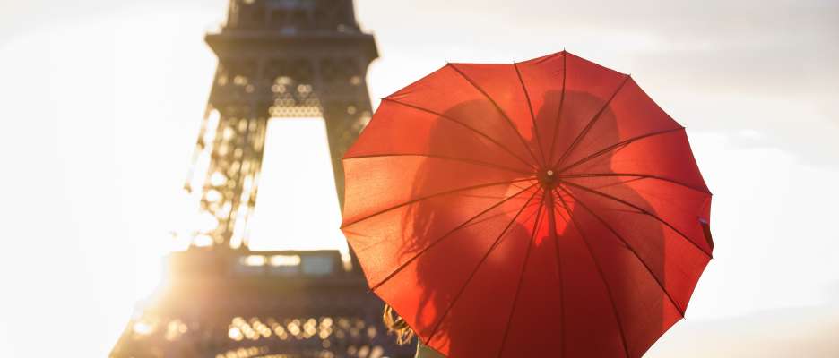 Baiser romantique à la tour Eiffel avec un parapluie roug en forme de cœur au lever du soleil