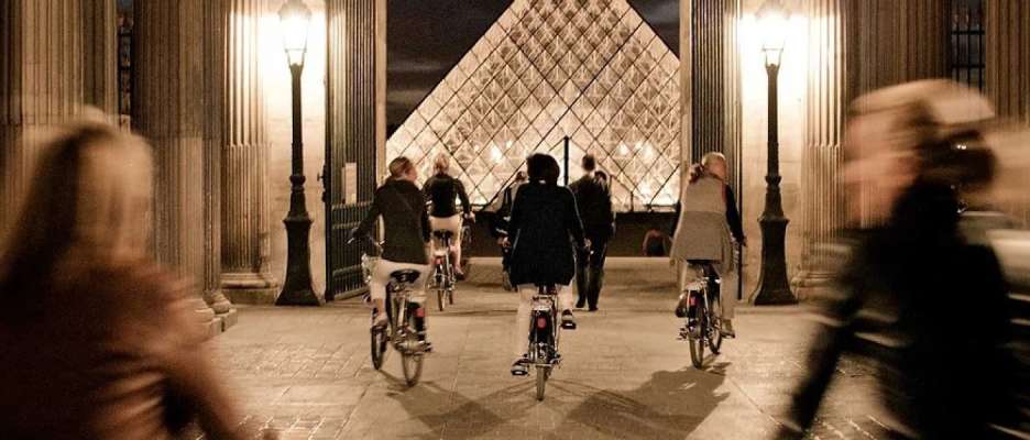 Group cycling at night past the Great Pyramid of the Louvre, Paris