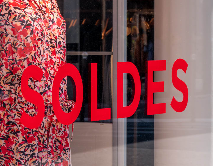 Close-up of a “SOLDES” sign written in French in red capital letters on the window of a clothing store in Paris, France, during the sales season