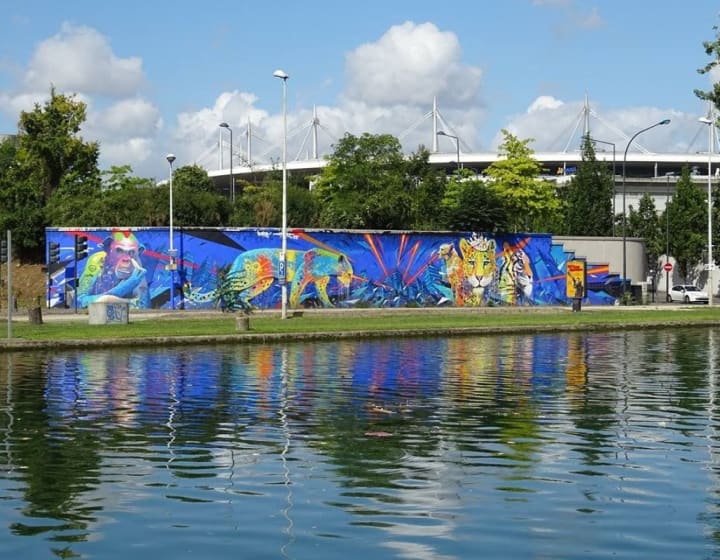 Street art fresco on the banks of the Saint-Denis canal, with the Stade de France in the background.