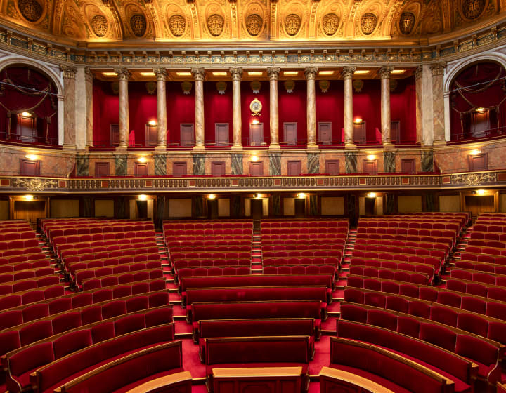 Intérieur majestueux de la Salle du Congrès de Versailles aux fauteuils en velours rouges, au colonnes en marbre et au décorations dorées au plafond