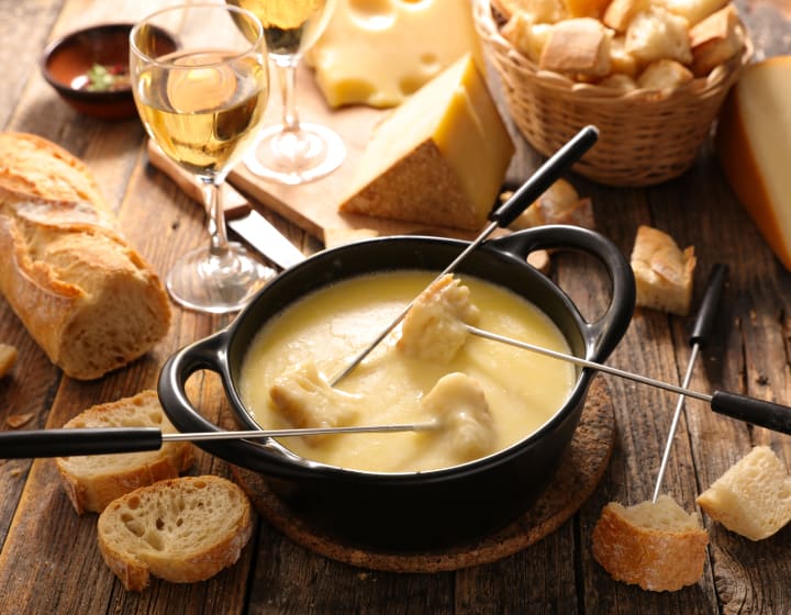 Table avec fondue au fromage, morceaux de pain et de fromage et un verre de vin blanc