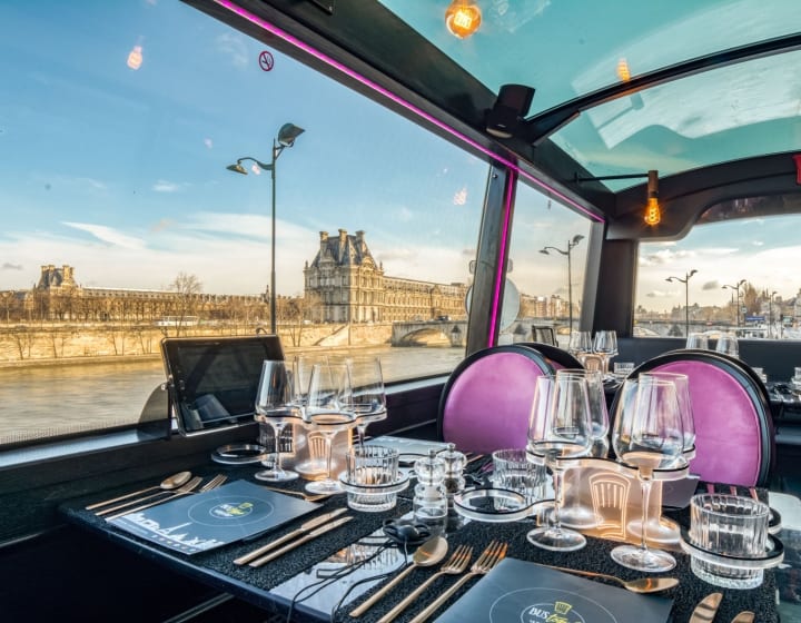 Table dressée à l&#039;étage d&#039;un bus Toqués roulant dans les rues de Paris avec une vue sur la Seine et sur le  musée du Louvre.