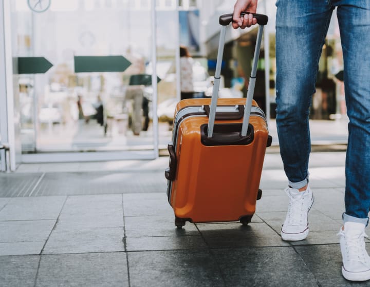 Man pulling an orange suitcase through a hall before his trip