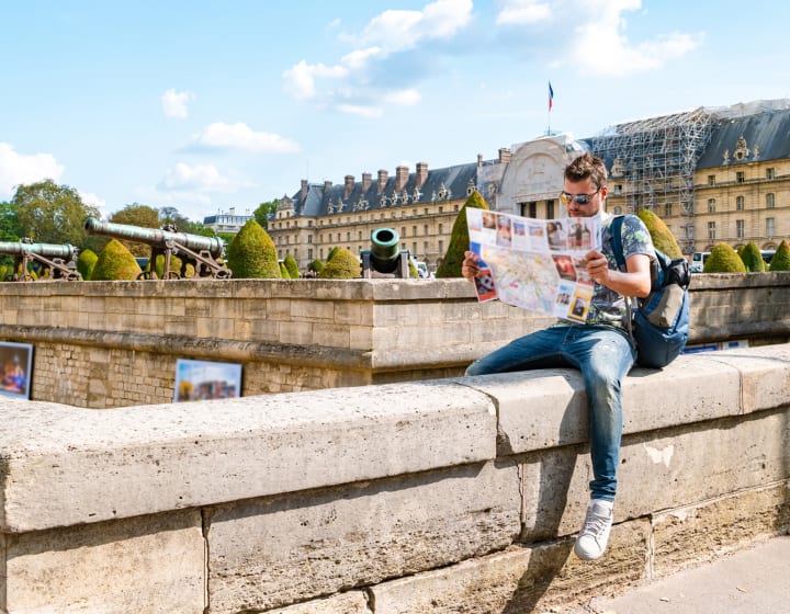 Young man looking at a map of Paris sitting astride a wall ledge