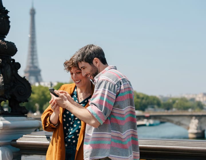 Couple looking at a telephone on a bridge over the Seine with the Eiffel Tower in the background