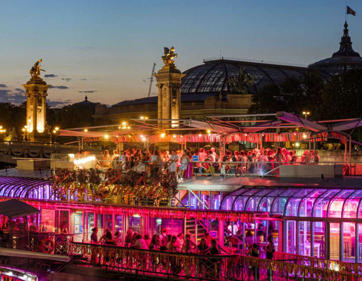 Guinguette Rosa Bonheur sur Seine animée et illuminée de nuit avec le point Alexandre III et le Grand Palais en arrière plan