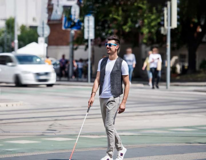 Young blind man with white cane walking across the street in city