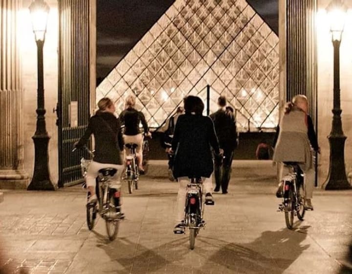 Group cycling at night past the Great Pyramid of the Louvre, Paris