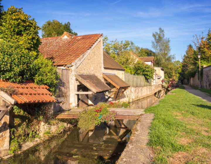 Paysage avec maisons, le long d'un cours d'eau avec petits pont d'accès et chemin de randonnée