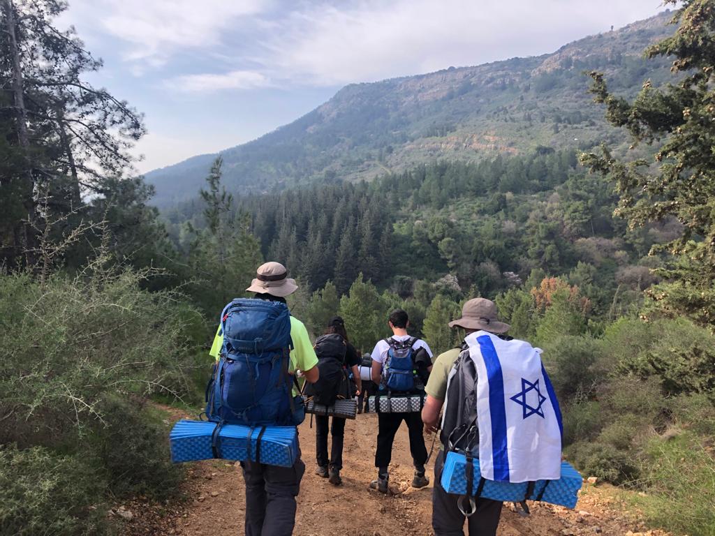 Three participants carrying a white rod outdoors with green trees in the background.