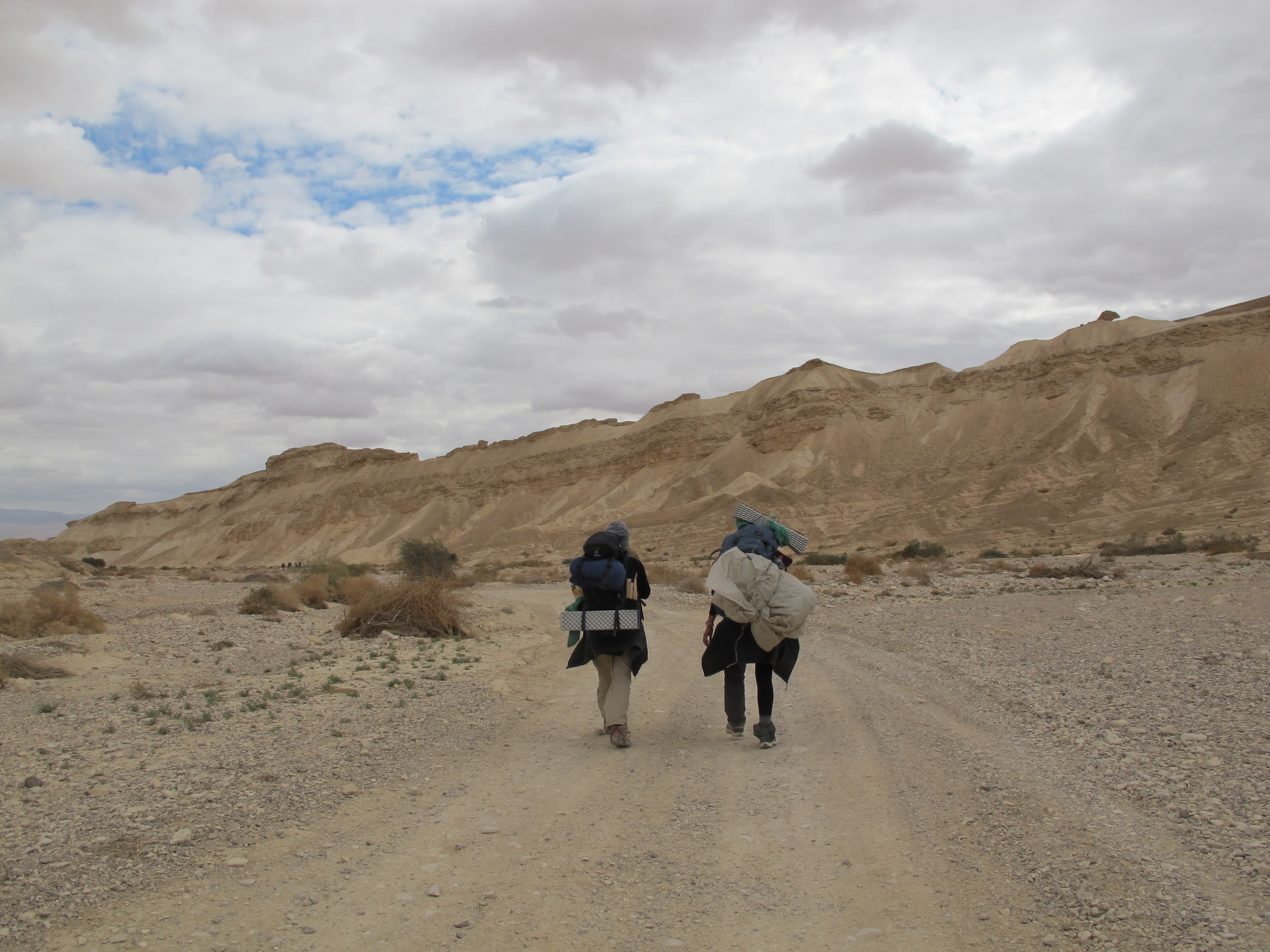 2 Mechina participants backpacking in the desert on a path with a group of participants in the distance.