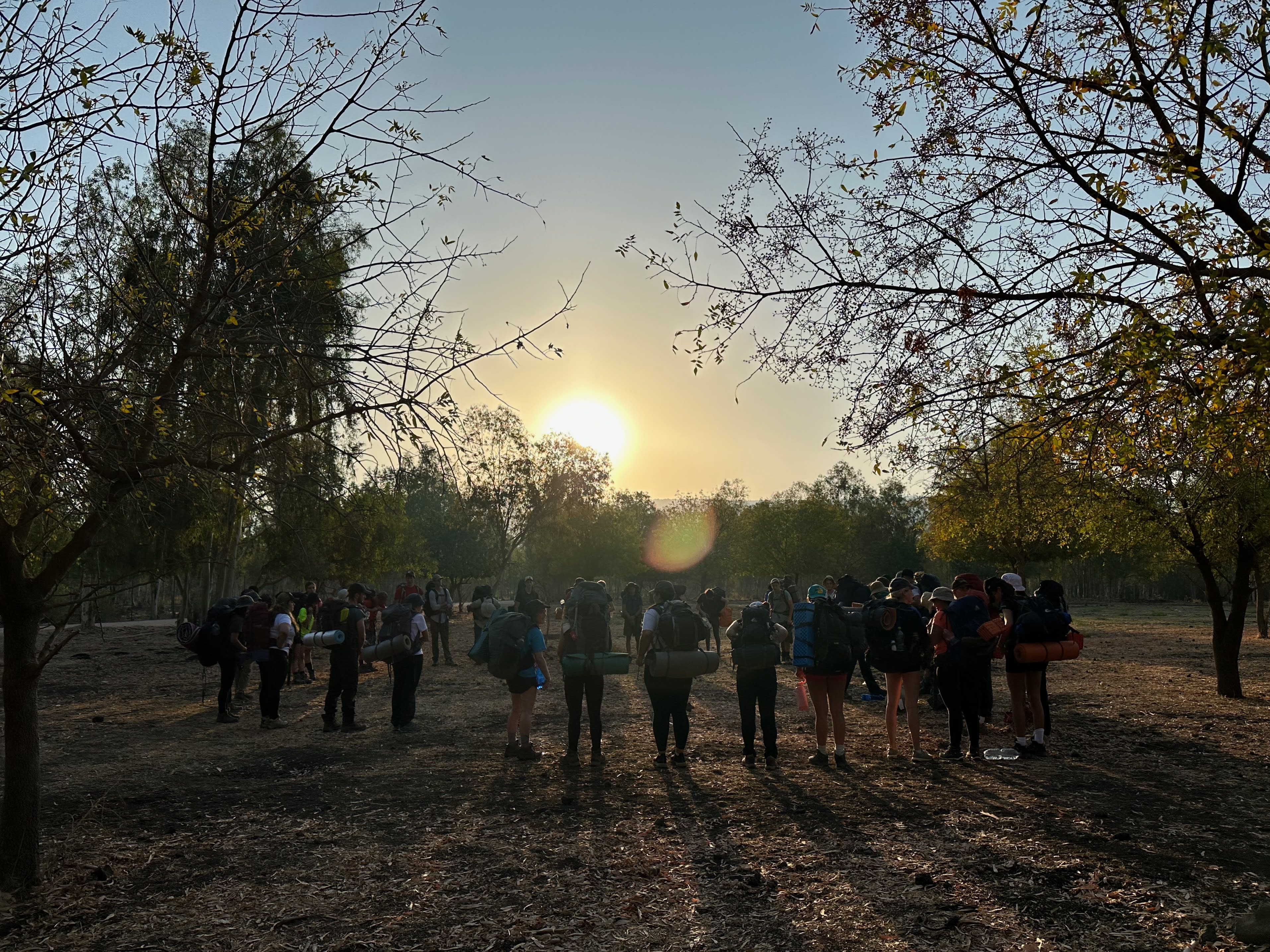 Participants standing outdoors in the sunrise with backpacks on and the sun behind them.