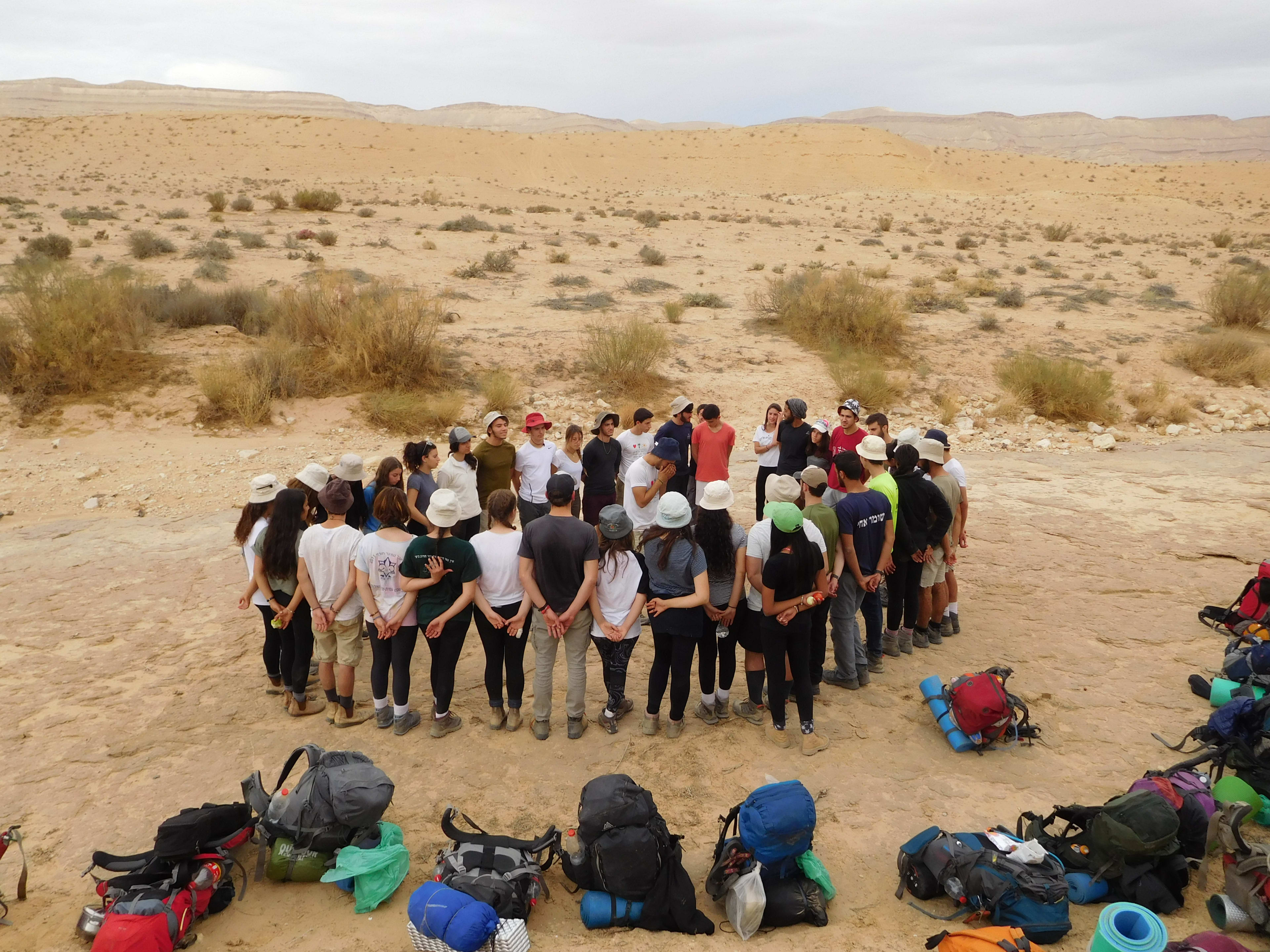 Mechina participants standing in a circle in the dessert with hiking backpacks on the ground.