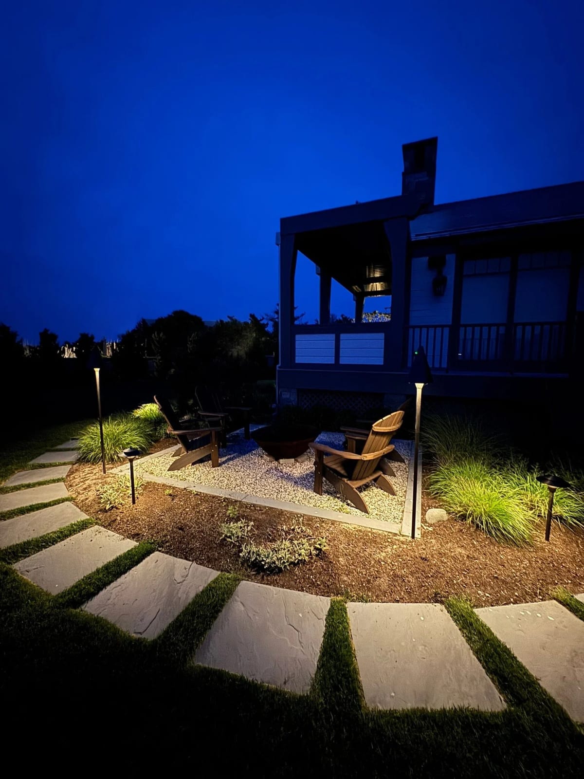 Warm outdoor lighting around a firepit seating area and garden path at dusk
