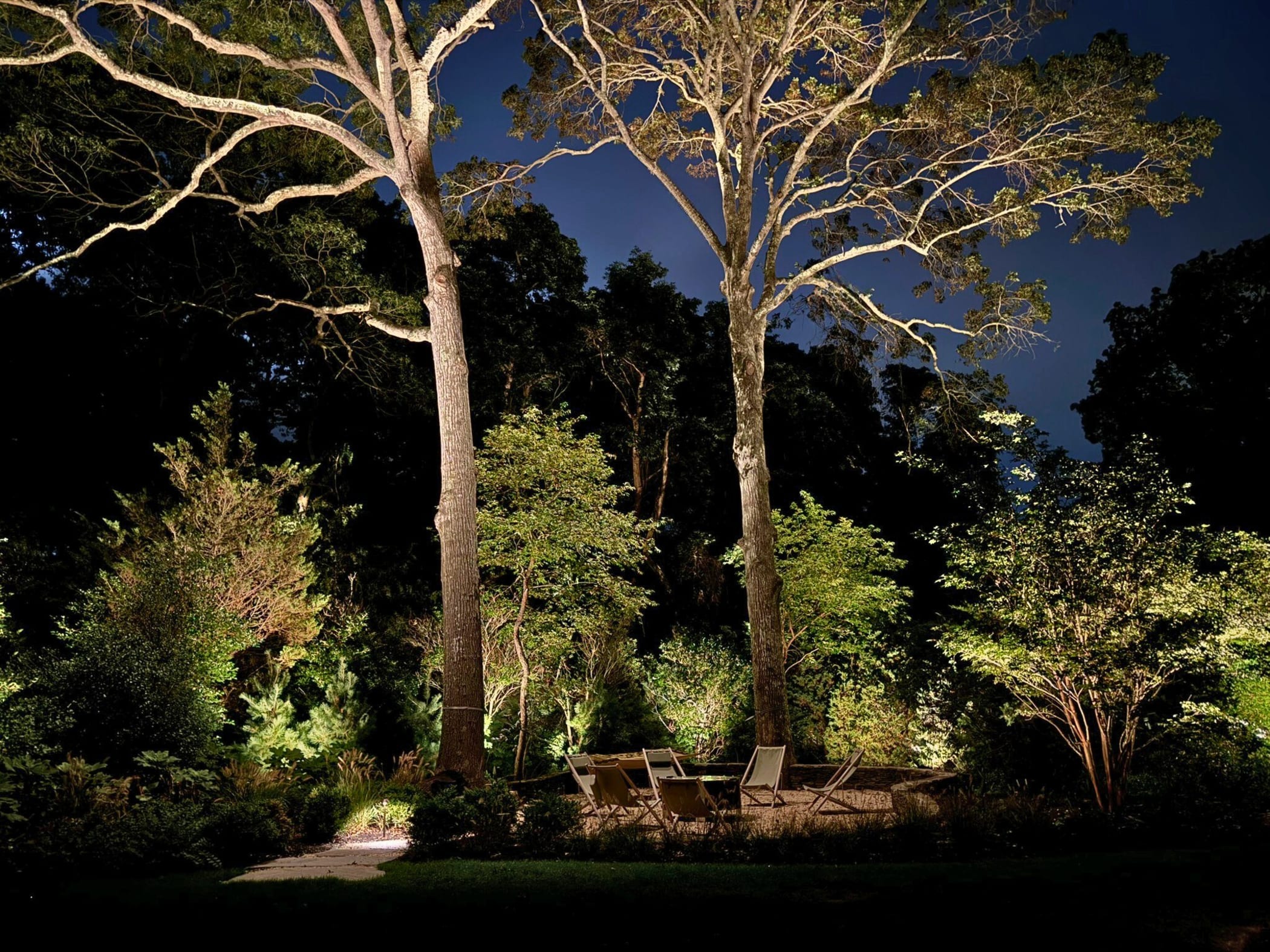 Architectural landscape lighting illuminating mature trees and an outdoor gathering area at an Amagansett estate