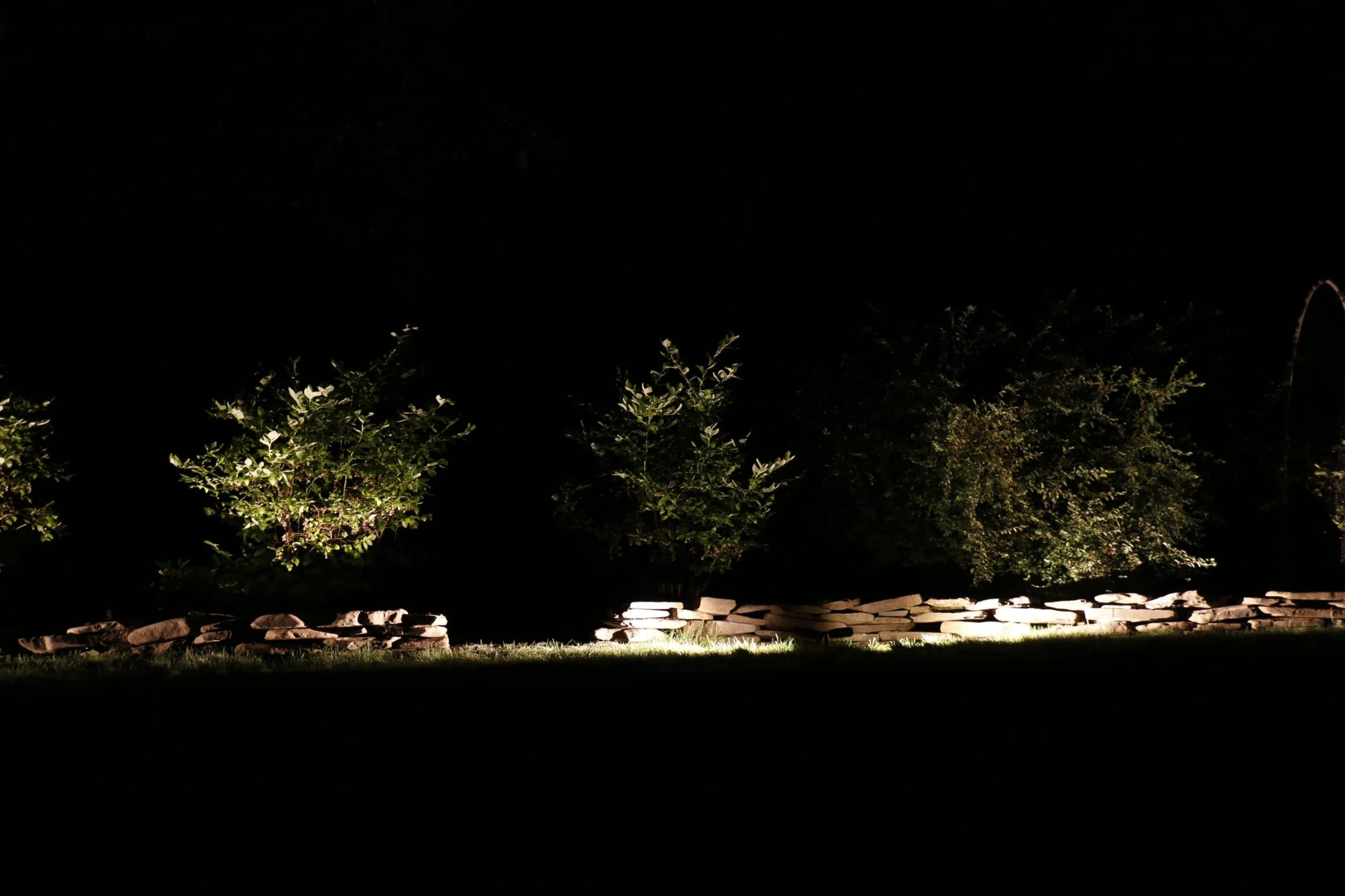 Subtle landscape lighting on stone walls and mature planting at a Hamptons estate