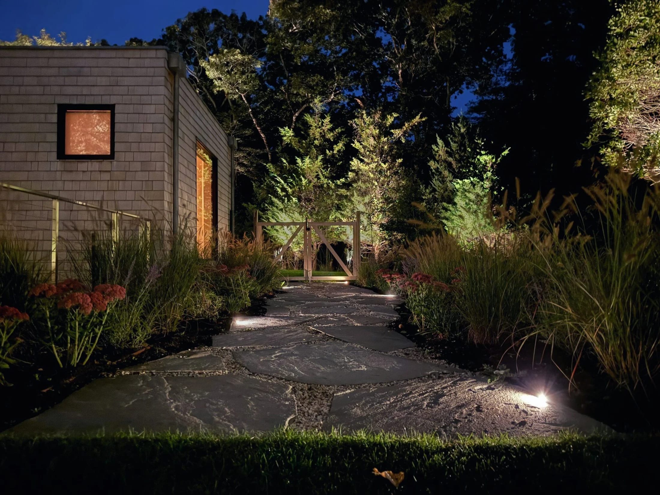 Thoughtfully illuminated stone pathway and garden gate at a Hamptons property after dark