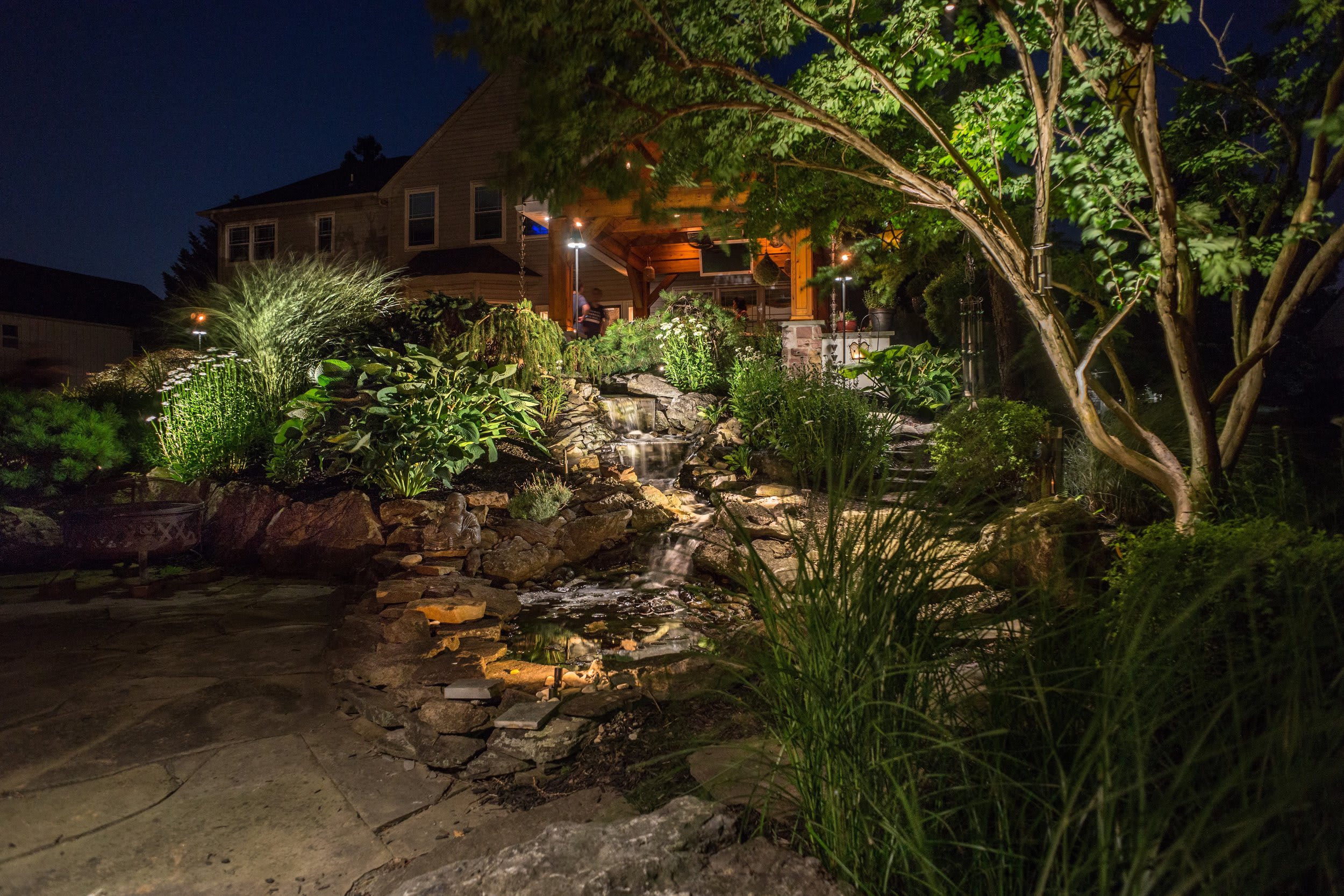 Warm low-glare lighting highlights planting and stonework beside a water feature