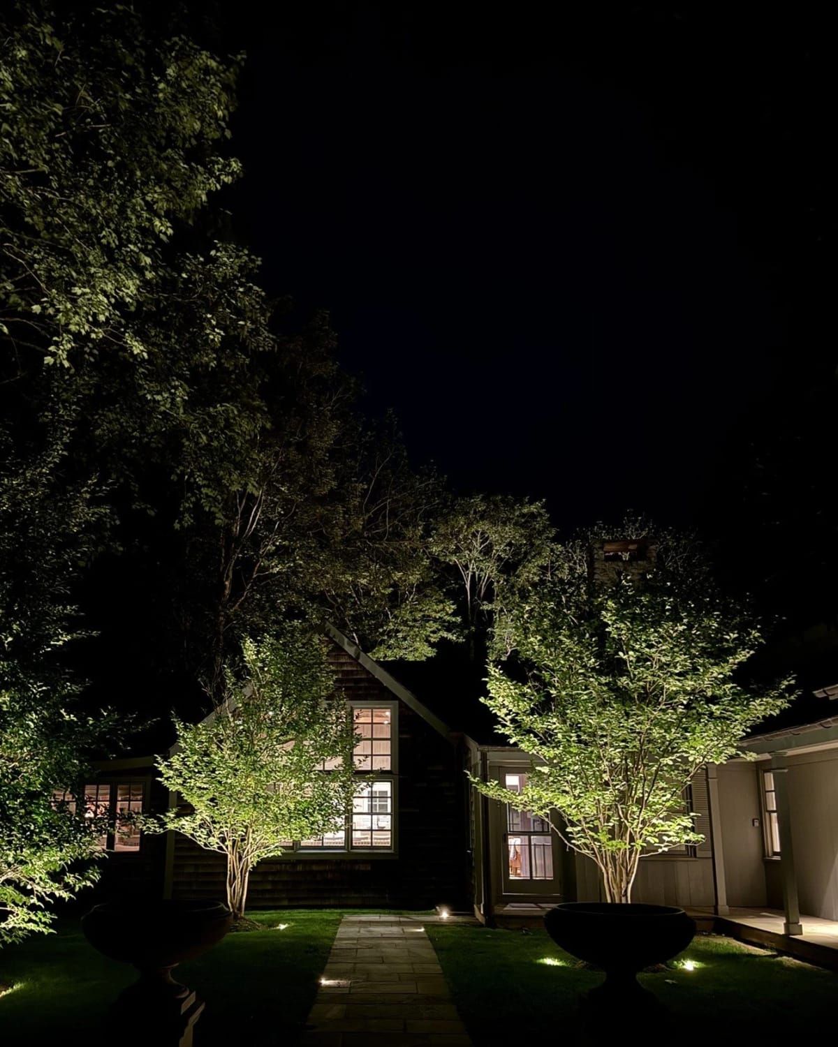 Layered landscape lighting creating depth through trees and garden areas