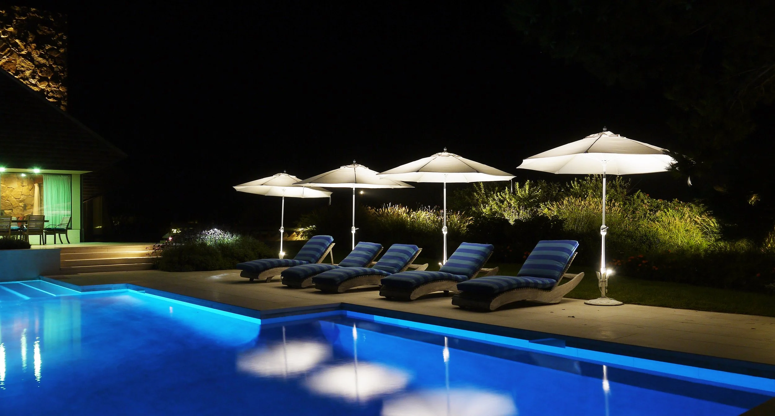 Warm, restrained landscape lighting surrounding a pool at a Hamptons home