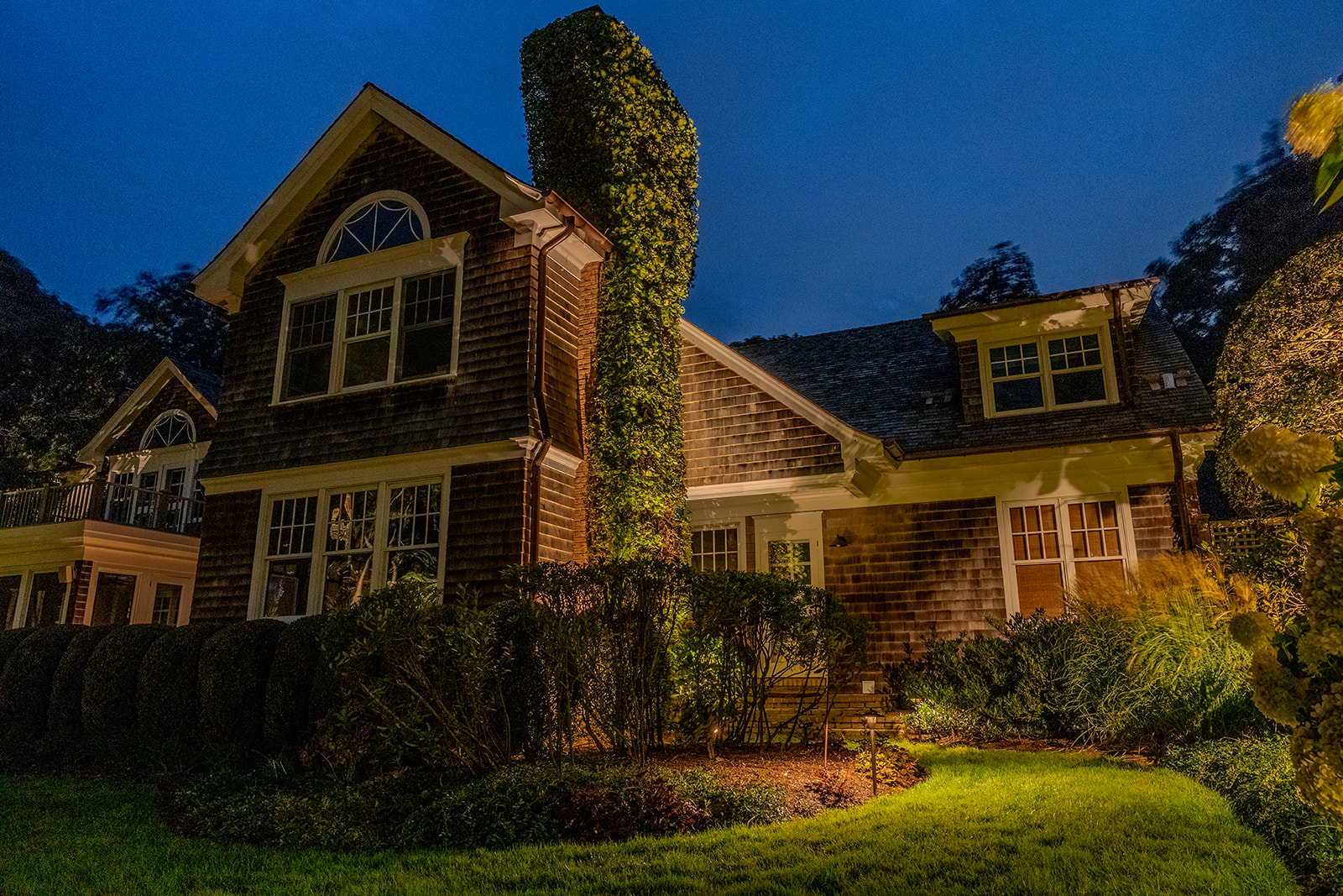 Modern shingle-style home with warm exterior landscape lighting after dark