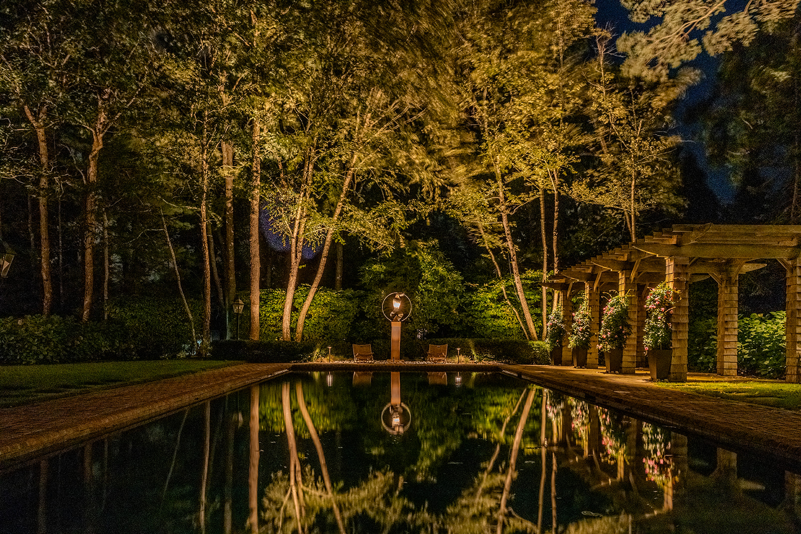 Illuminated pergola and mature trees reflected in a swimming pool at night in Quogue