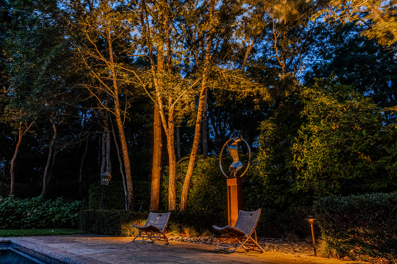 Garden sculpture framed by illuminated tree trunks and surrounding foliage in Quogue