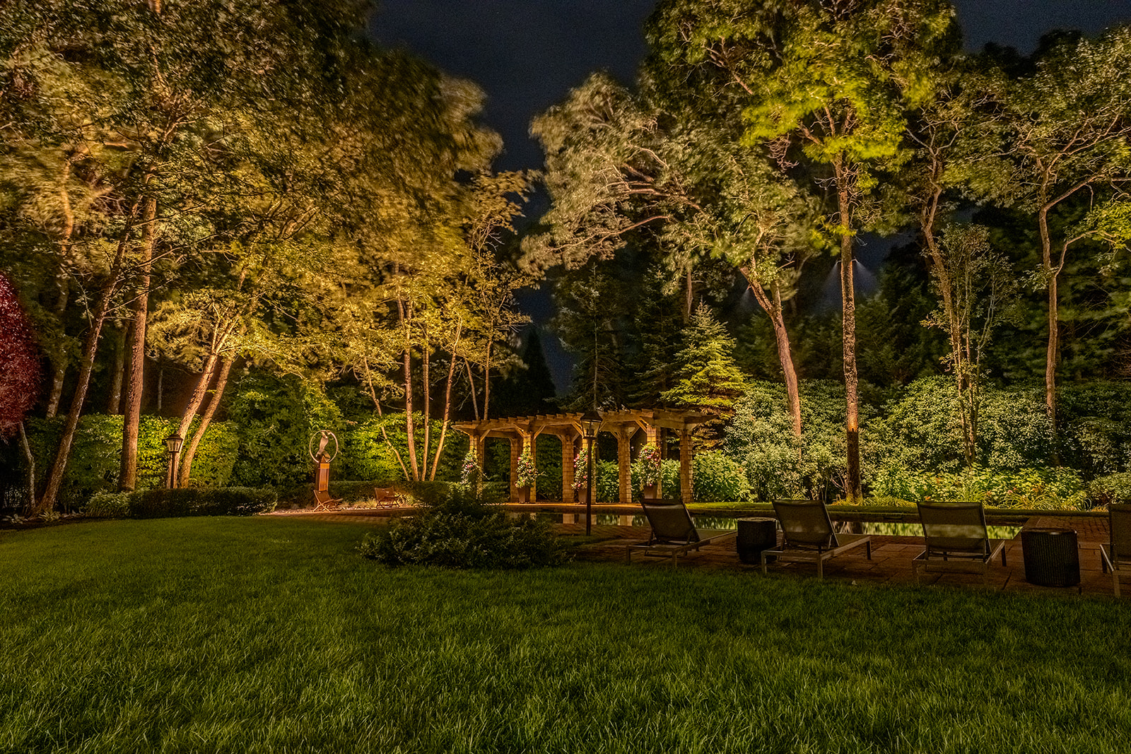 Panoramic nighttime landscape with illuminated trees and pergola across a Quogue lawn