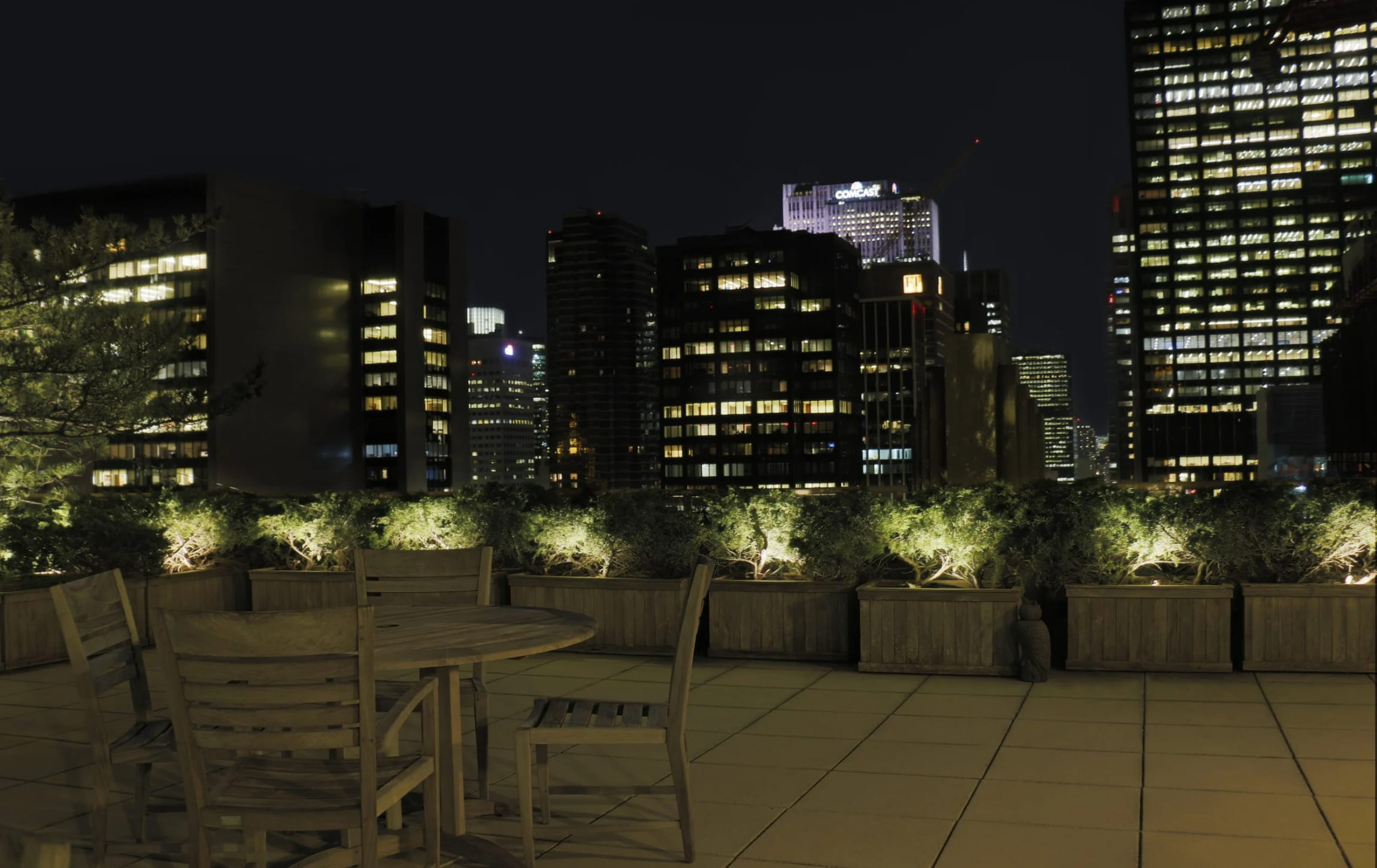 An outdoor terrace and garden illuminated at night beyond a home’s interior spaces
