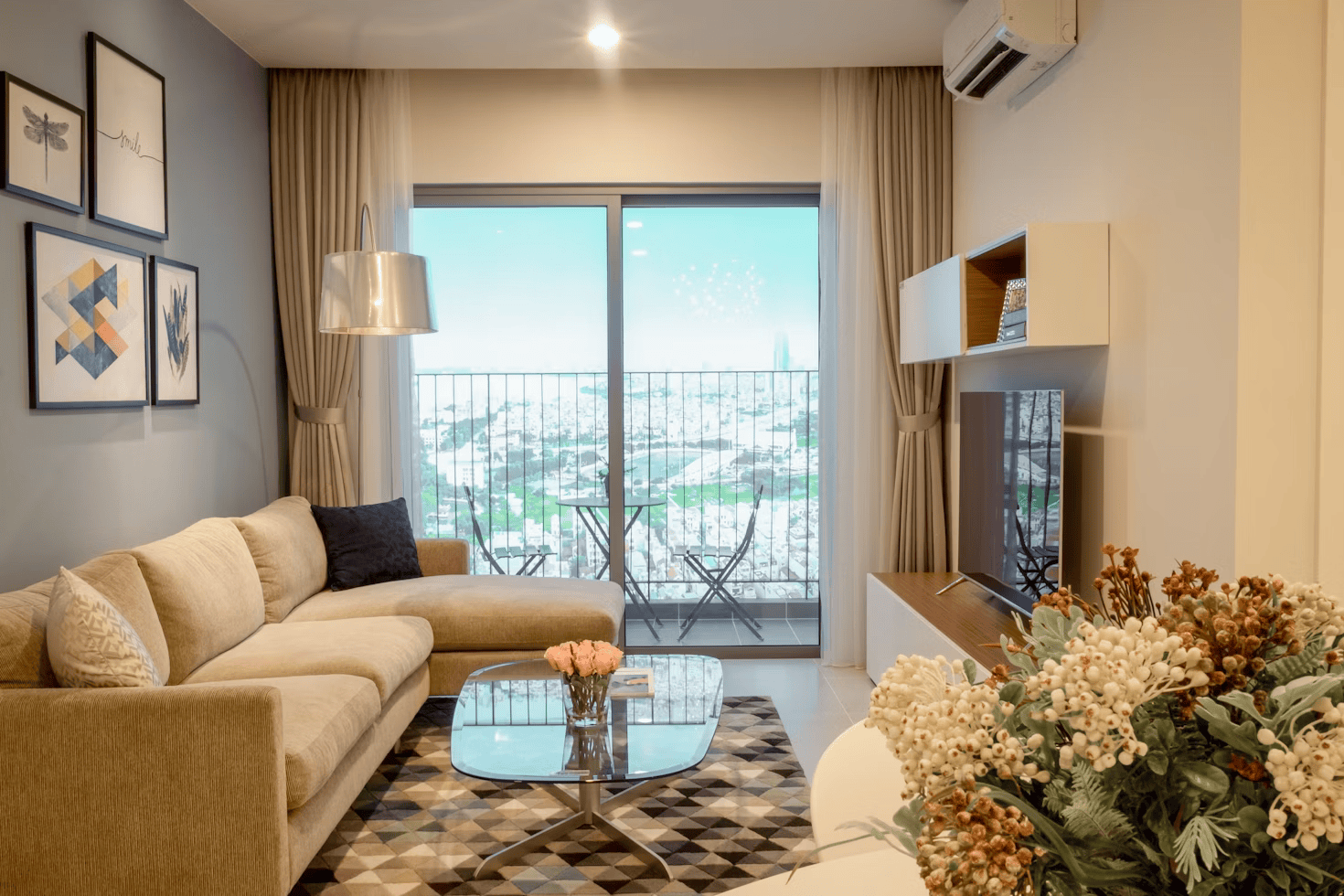 Discover the elegance of a modern living room with a beige sofa, glass coffee table, and geometric rug. Large windows with cityscape views complement the art-adorned walls. Perfectly curated for home spaces, lush plants and ambient ceiling lights complete this interior design masterpiece.