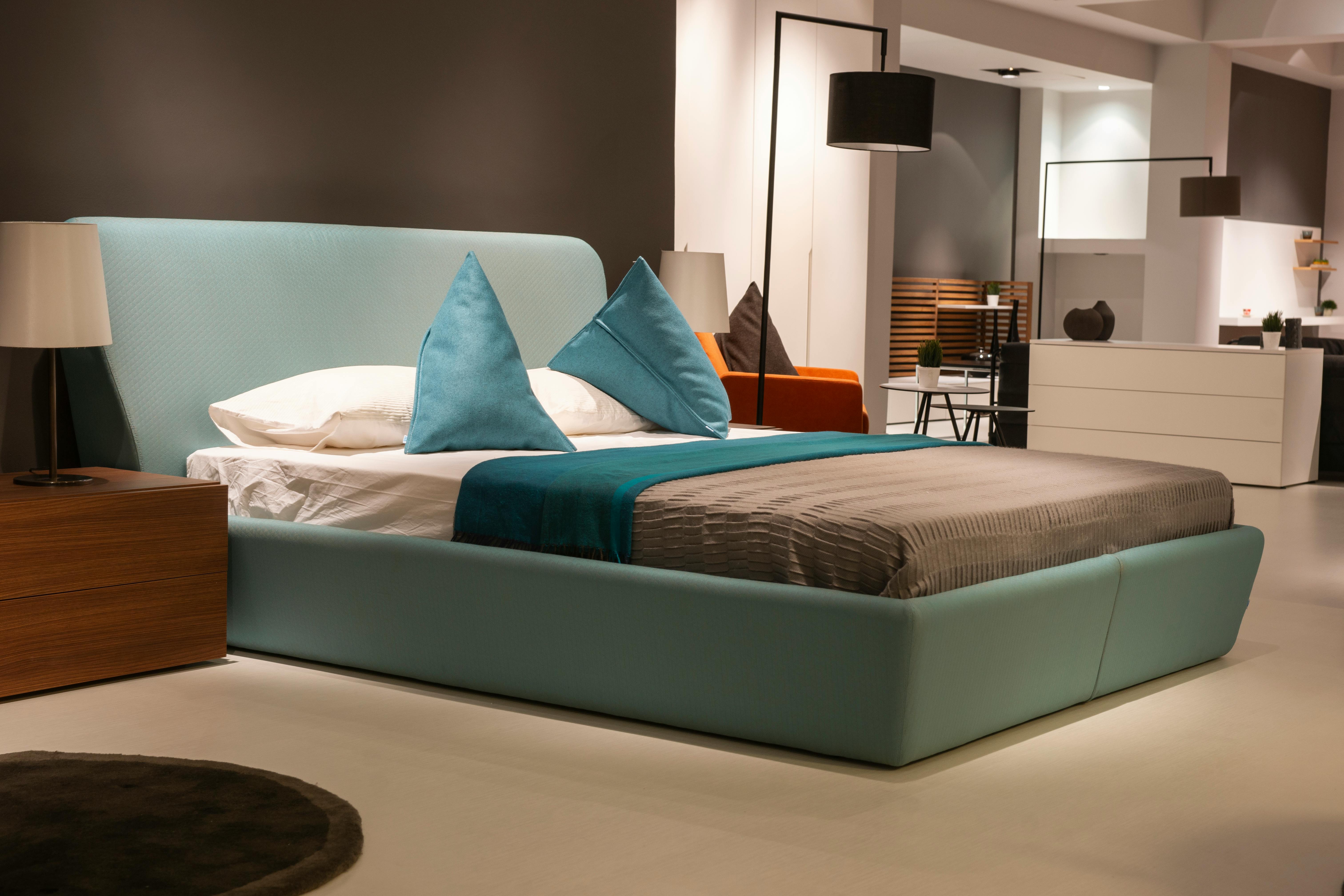 Modern bedroom with a light blue upholstered bed, gray bedding, and teal throw pillows. Flanked by wooden nightstands and lamps, this home space features minimalist decor with contrasting walls and sleek furnishings—perfect inspiration from expert interior design services.