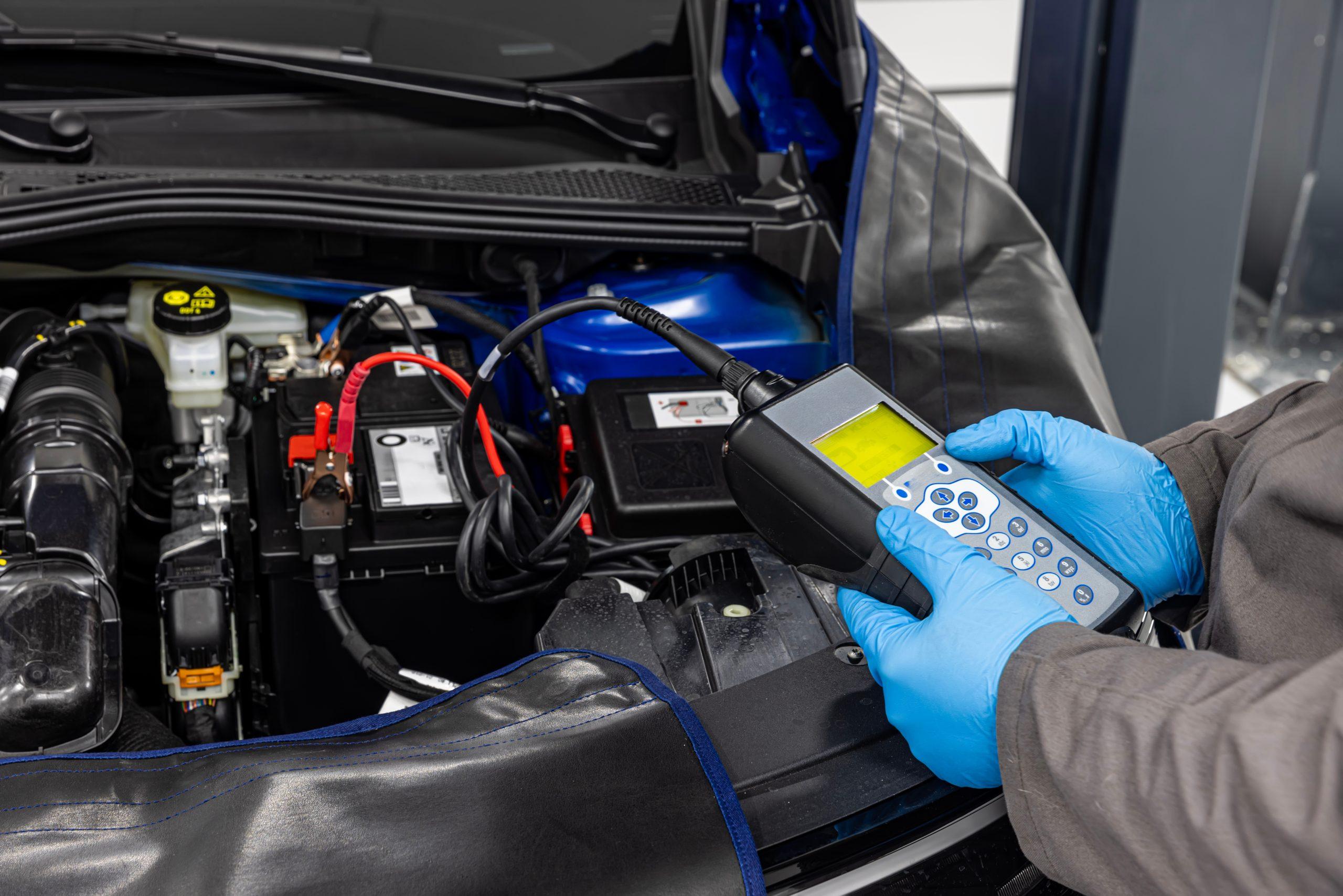 Technician testing the 12V auxiliary battery in a hybrid car