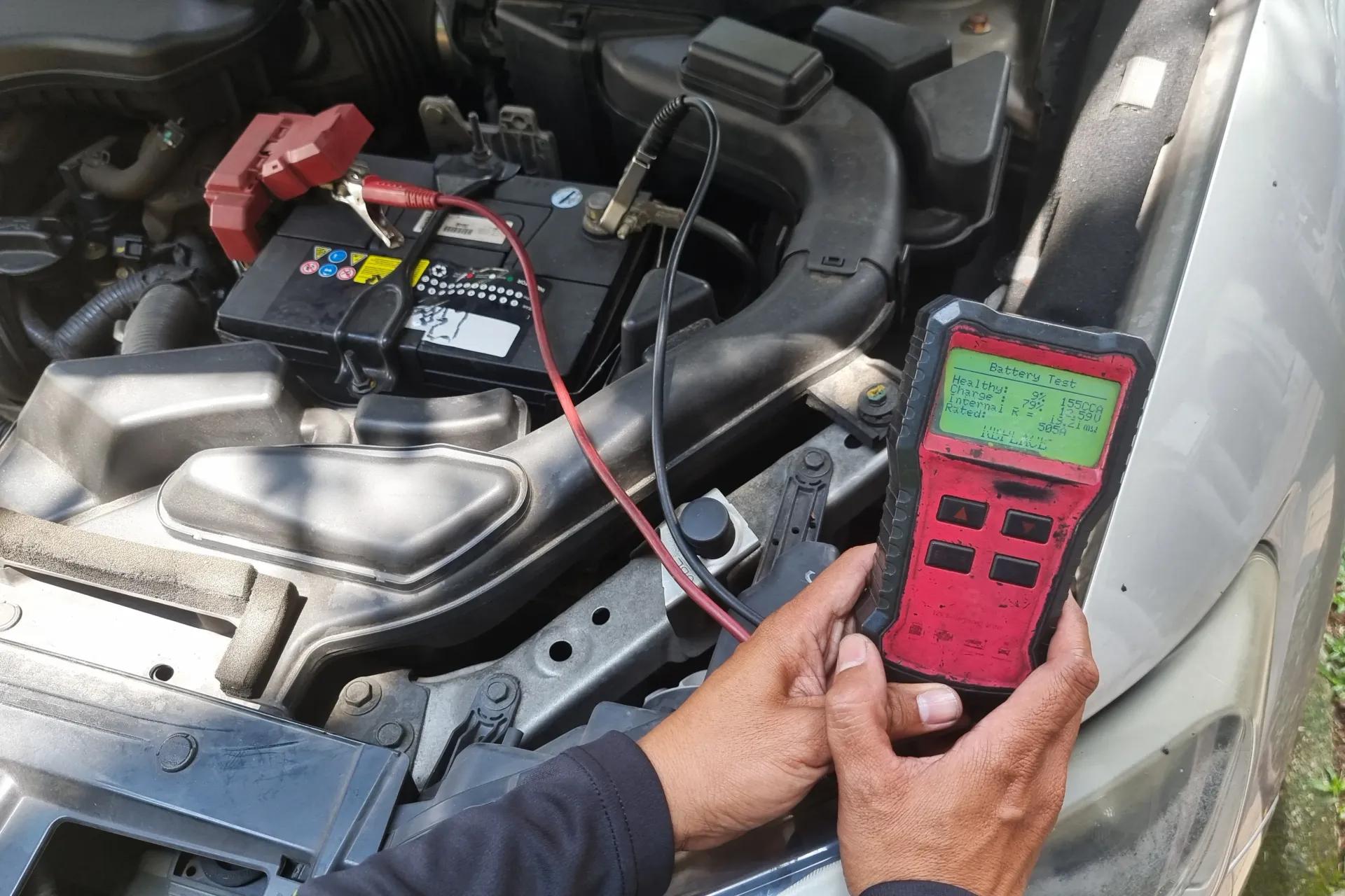 Technician testing a car battery with a digital battery diagnostic tester