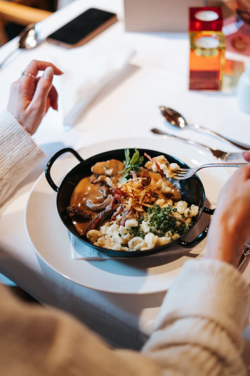 A person enjoying a hearty meal at Glemmtalerhof, with delicious dumplings and sauce in a cozy setting.