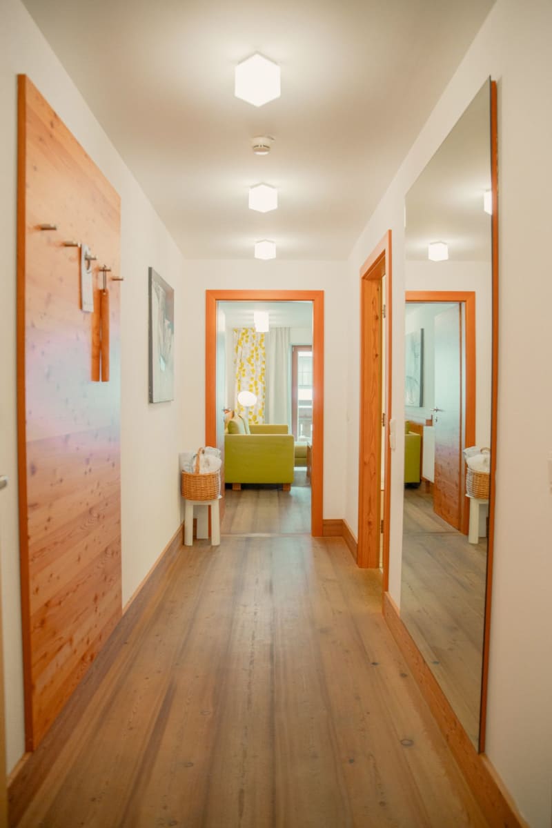 Ein heller Flur im Glemmtalerhof in Hinterglemm mit einem gemütlichen Wohnzimmer im Hintergrund. DE