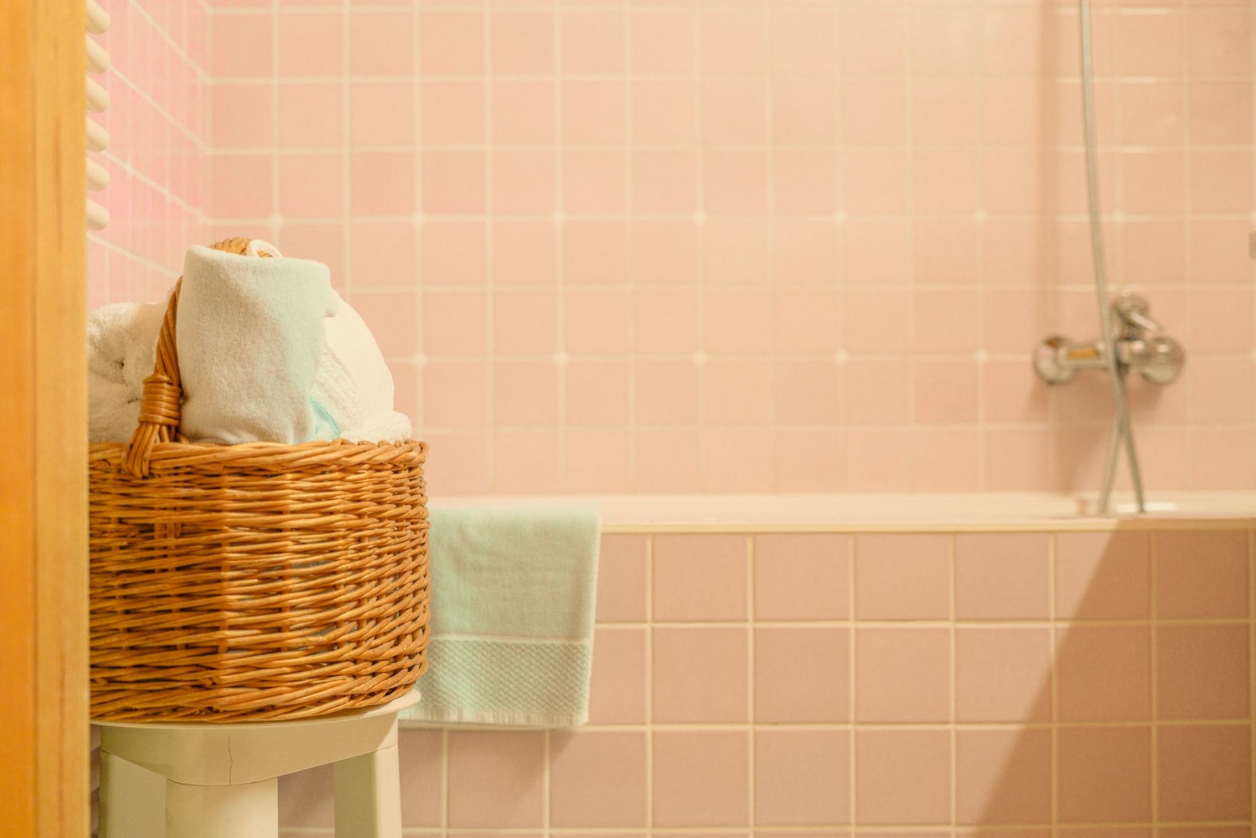 Ein gemütliches Badezimmer mit Handtüchern im Korb und sanften rosa Fliesen. DE