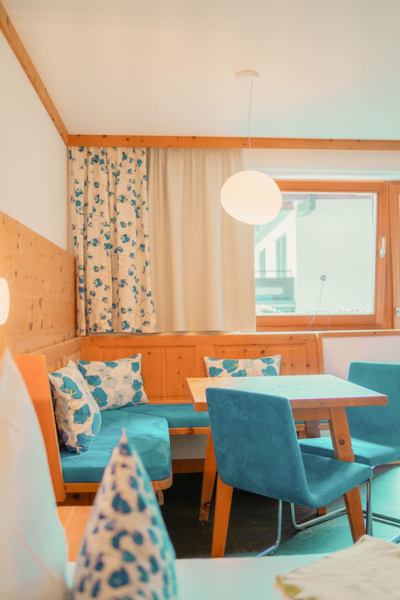 Gemütlicher Essbereich im Glemmtalerhof, modern eingerichtet mit blauen Akzenten und floralen Vorhängen.
