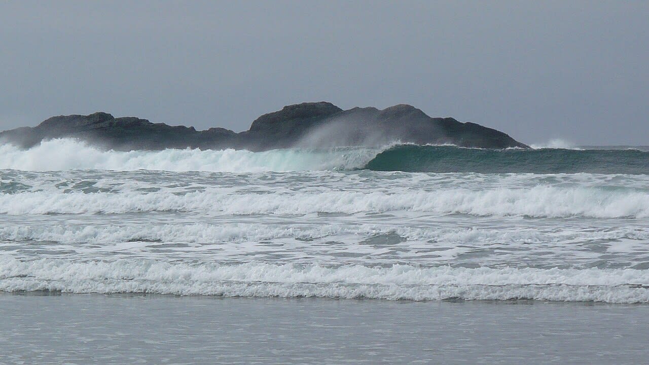 A large wave exploding white against a rocky headland