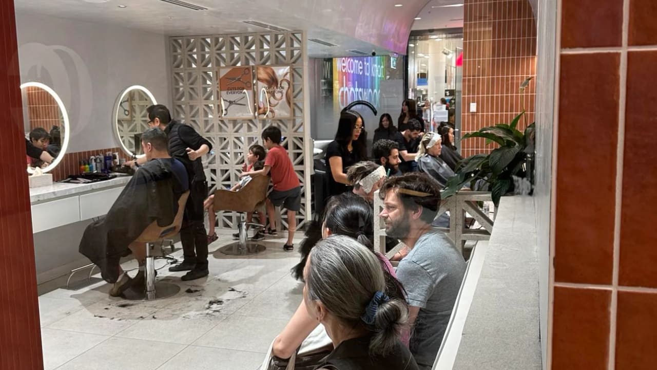 Inside Cuts Avenue Chatswood Chase on a busy afternoon, stylists cutting while customers wait on the bench, with Kmart across the walkway