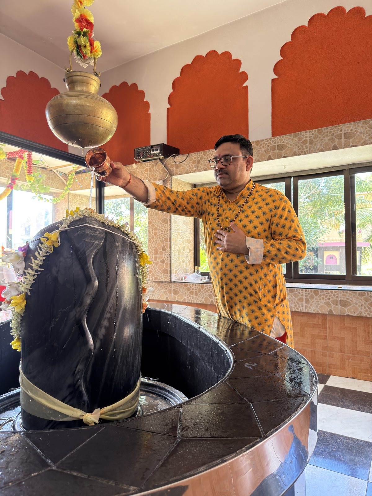 Acharya Amit Pandey performing a Shiva abhishekam, pouring sacred water over a garlanded lingam