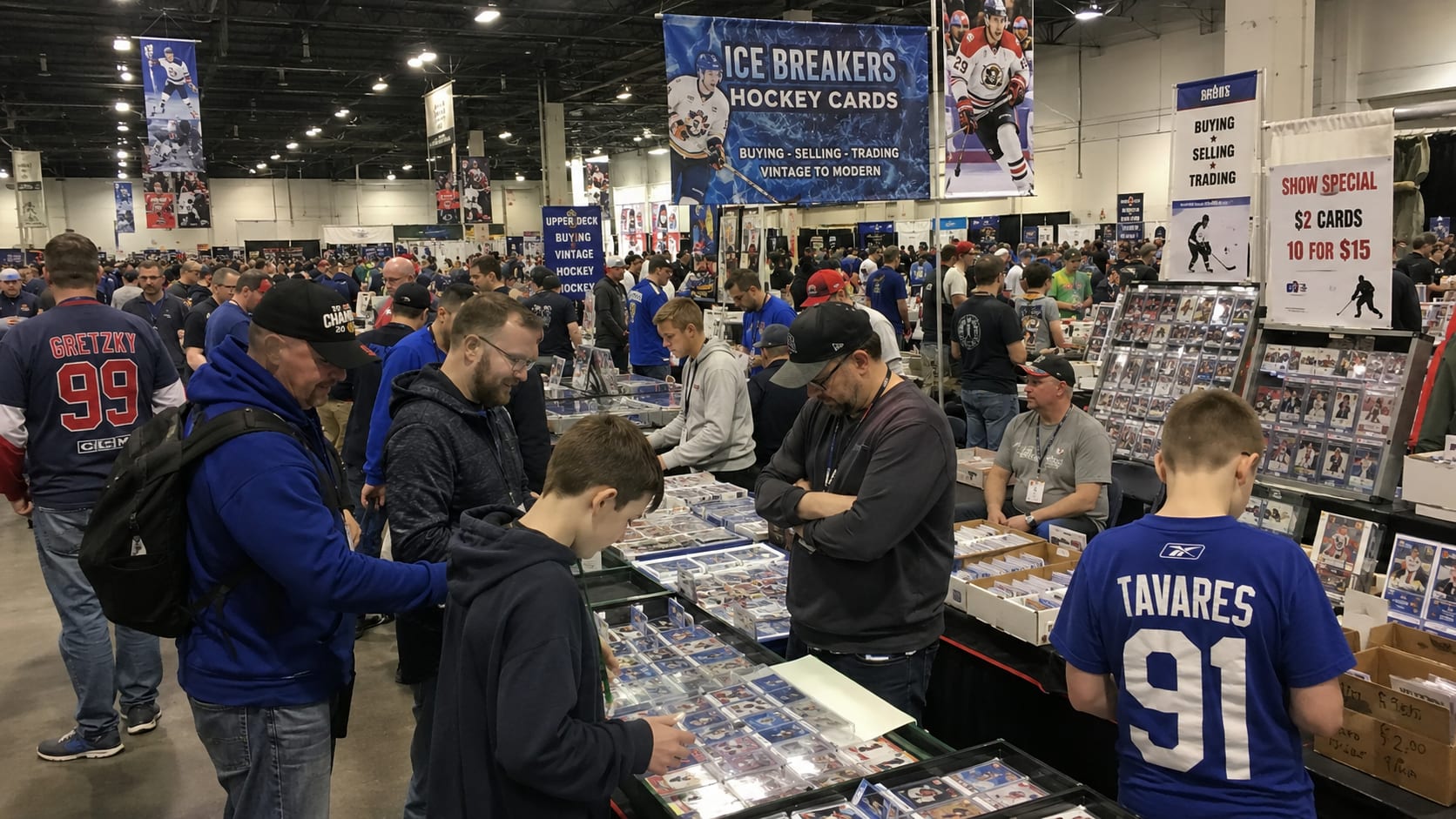 Busy hockey card show filled with collectors trading hockey cards, browsing showcases, negotiating deals, and interacting with other members of the hockey card community.