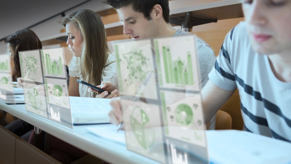 Group of people sitting along a desk working with notepads and facing digital screens with data on them